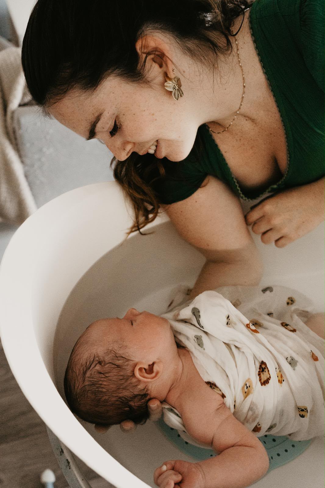 Une maman souriante penchée au-dessus de son bébé pendant le bain sensoriel