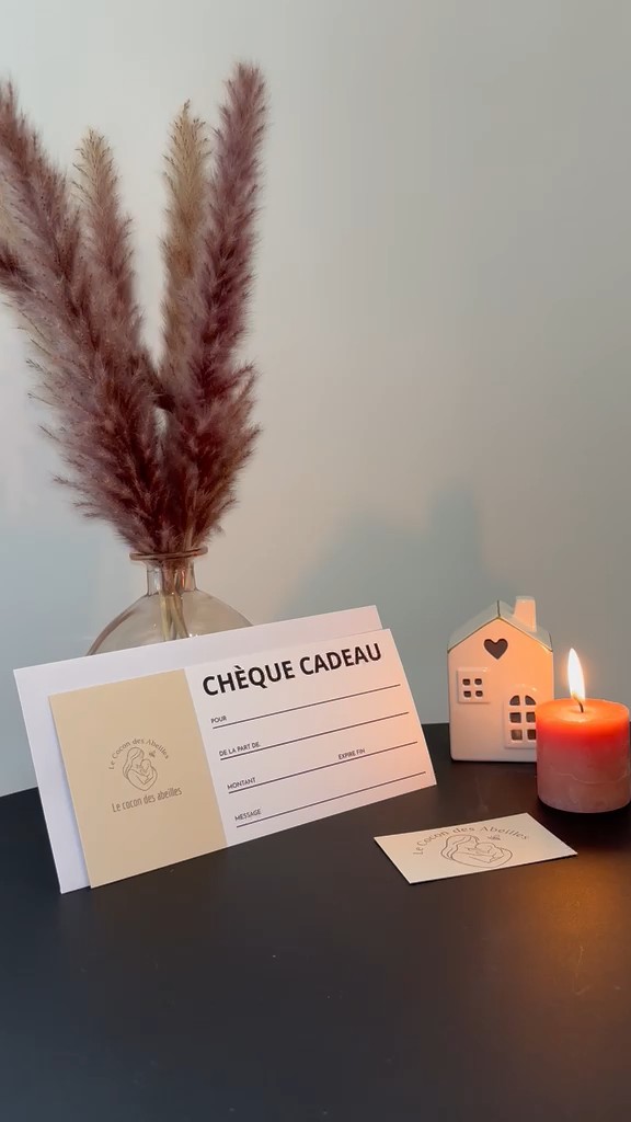 Chèque cadeau Le Cocon des Abeilles posé sur une table avec une bougie et des fleurs séchées